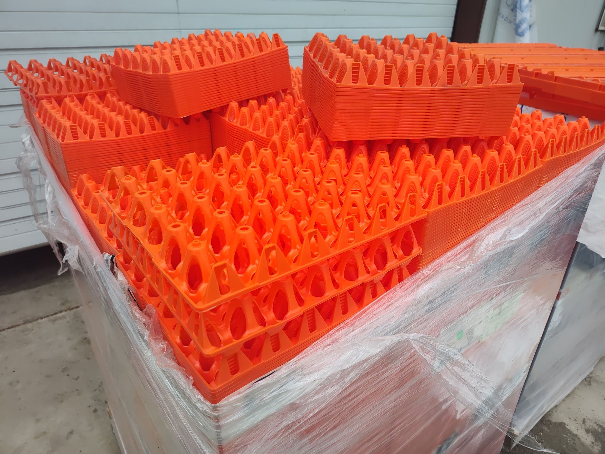 Shrink-wrapped pallet of orange plastic egg flats stacked in the shed