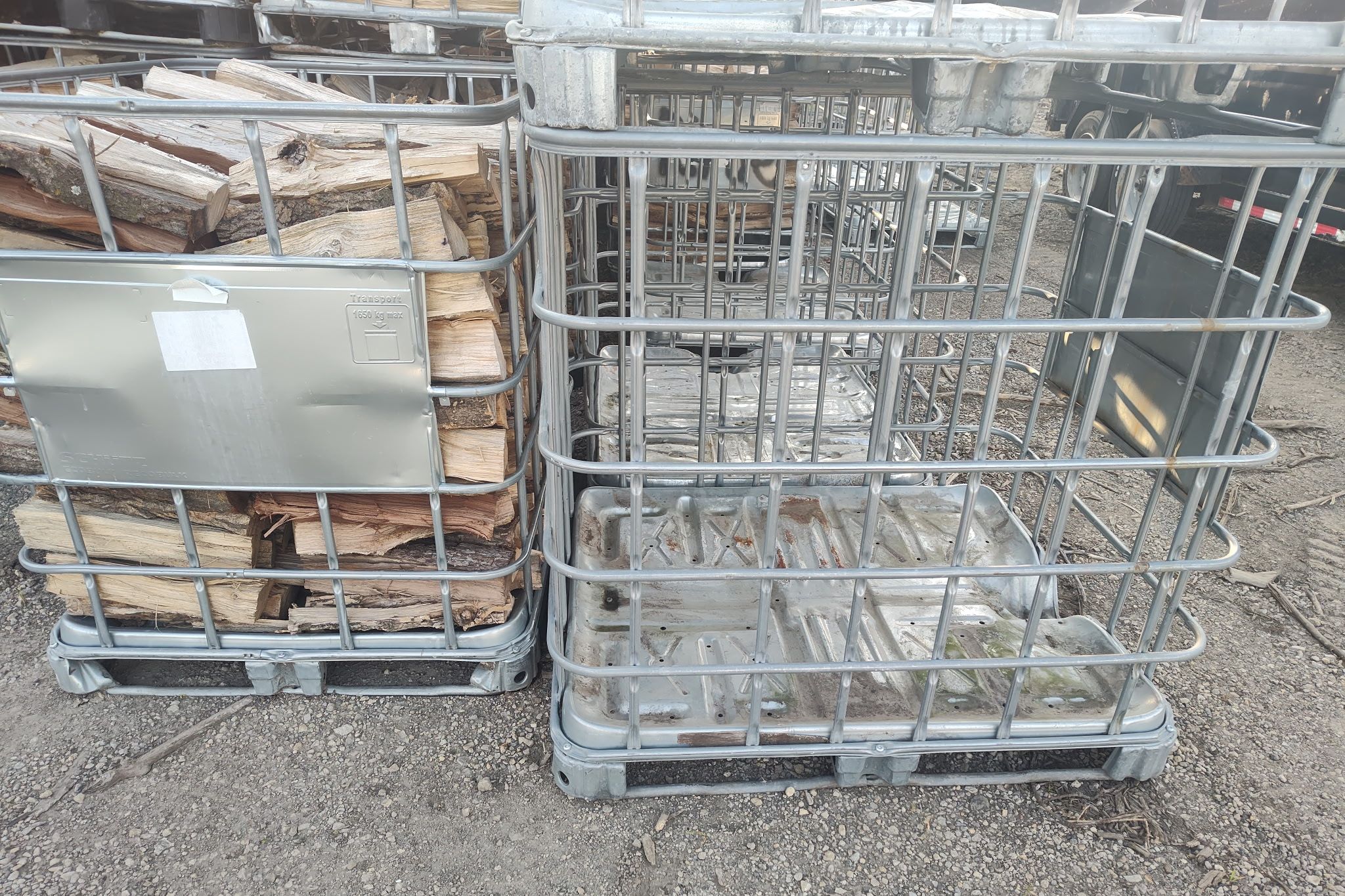 Empty galvanized IBC cage standing beside one packed with firewood
