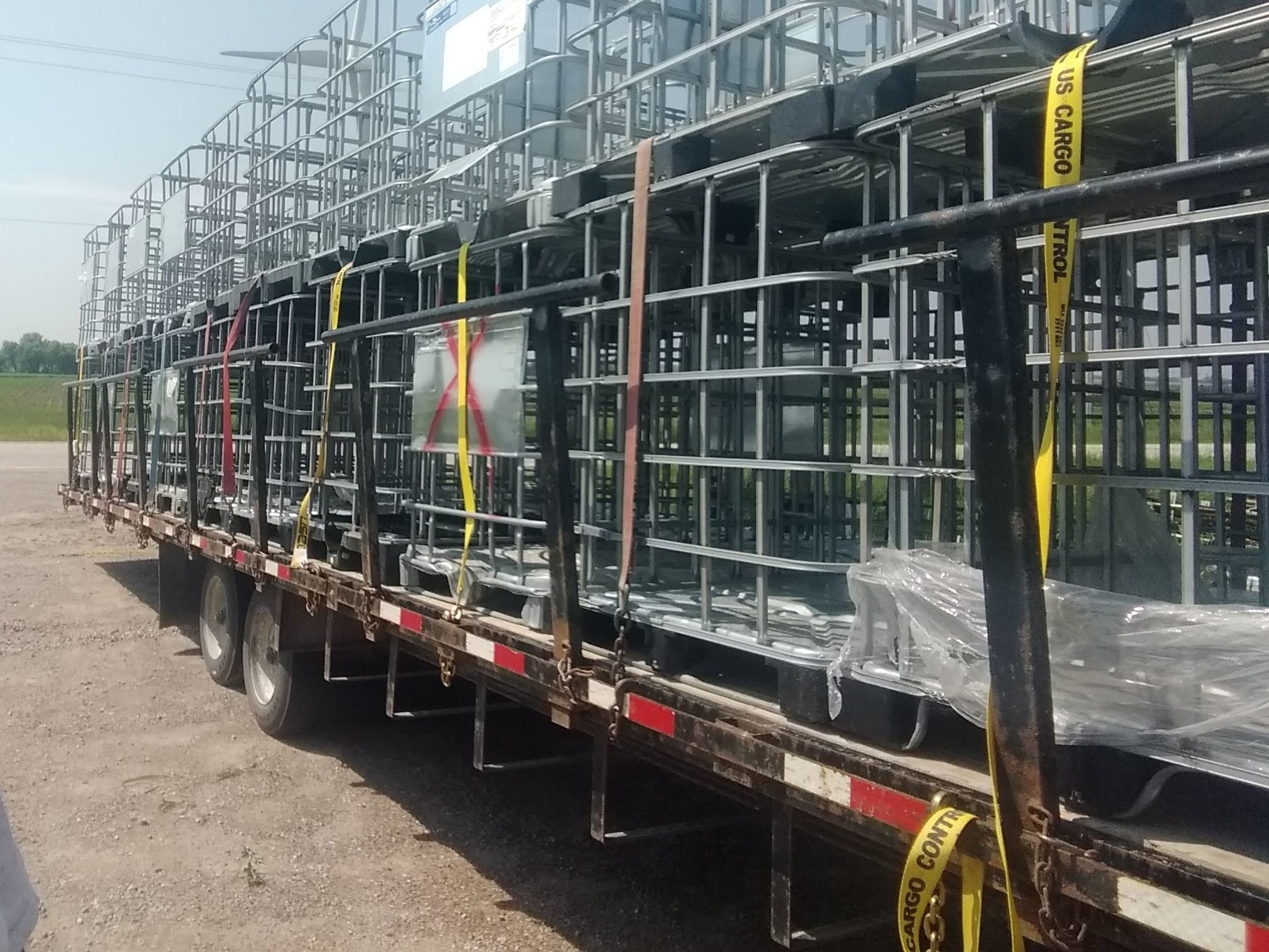 Flatbed trailer stacked and strapped with galvanized IBC cages ready to leave