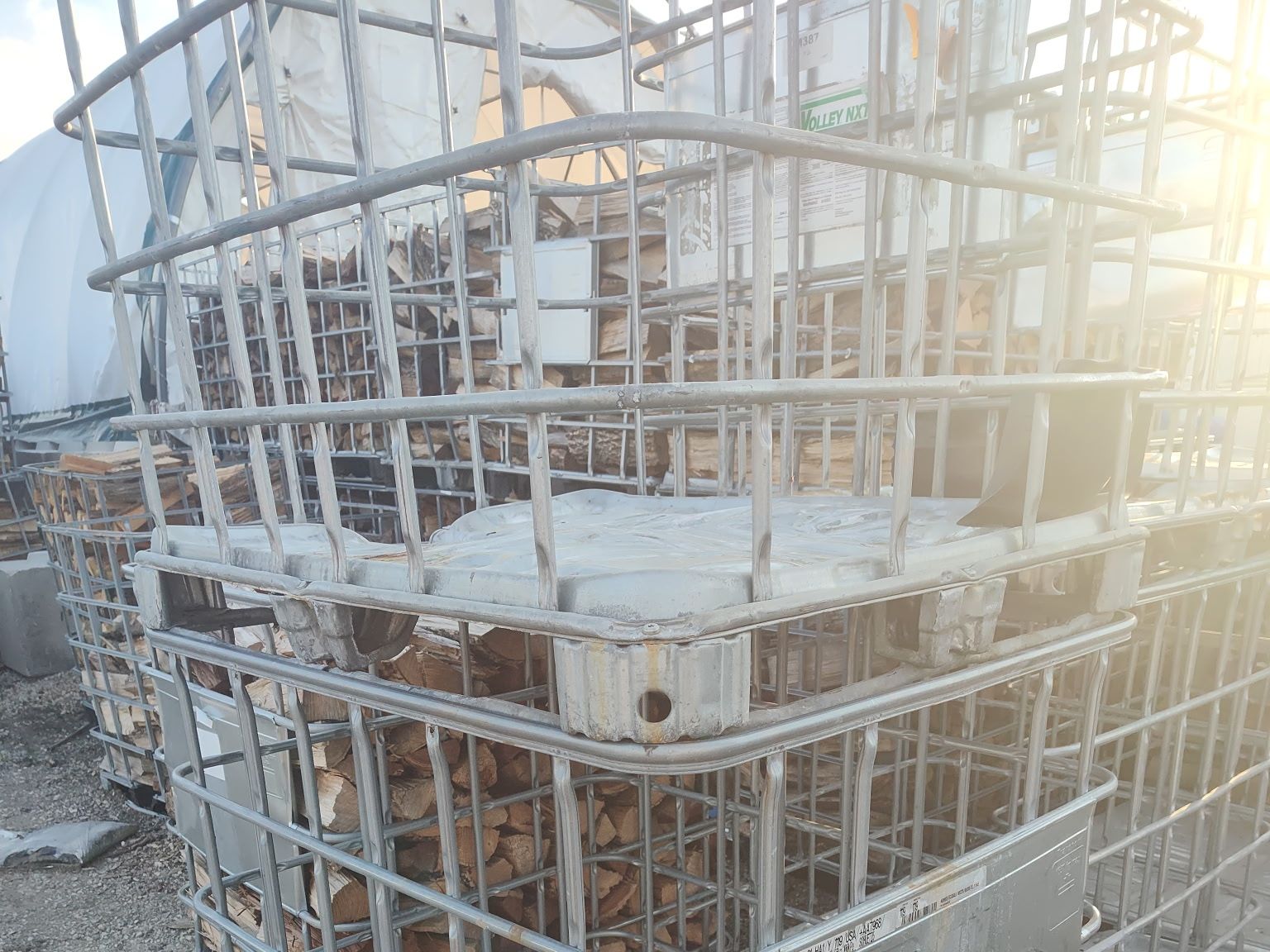 Rows of IBC cages filled with split firewood stacked in the yard