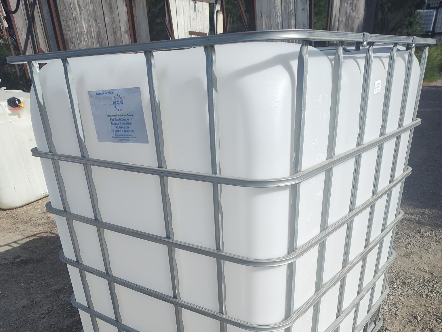 Single white 275 gallon IBC tote in its galvanized cage on a gravel lot