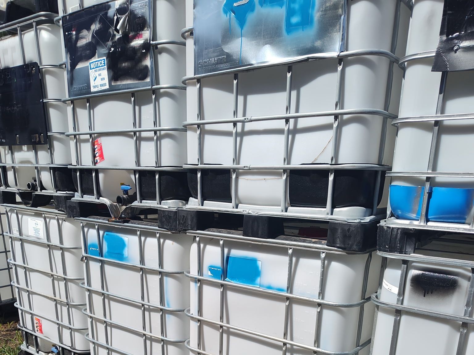 Stacked IBC totes lined up two high along the edge of the yard