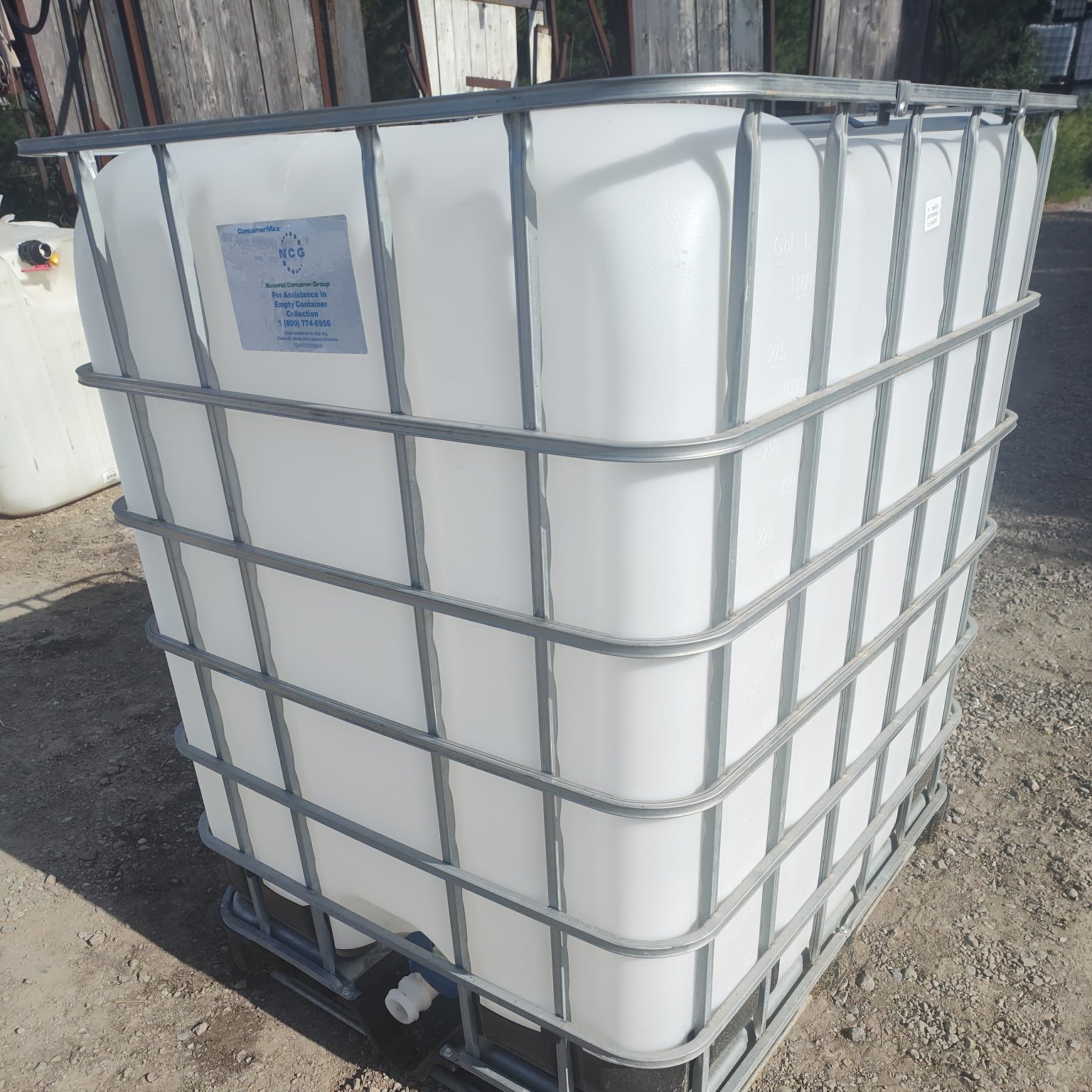 Single white 275 gallon IBC tote in a galvanized cage on a gravel lot