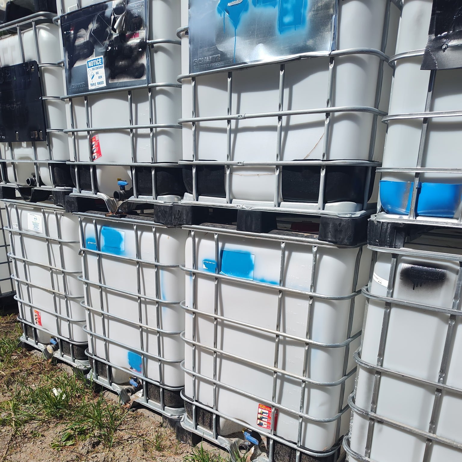 Row of white IBC totes stacked two high along the yard fence line